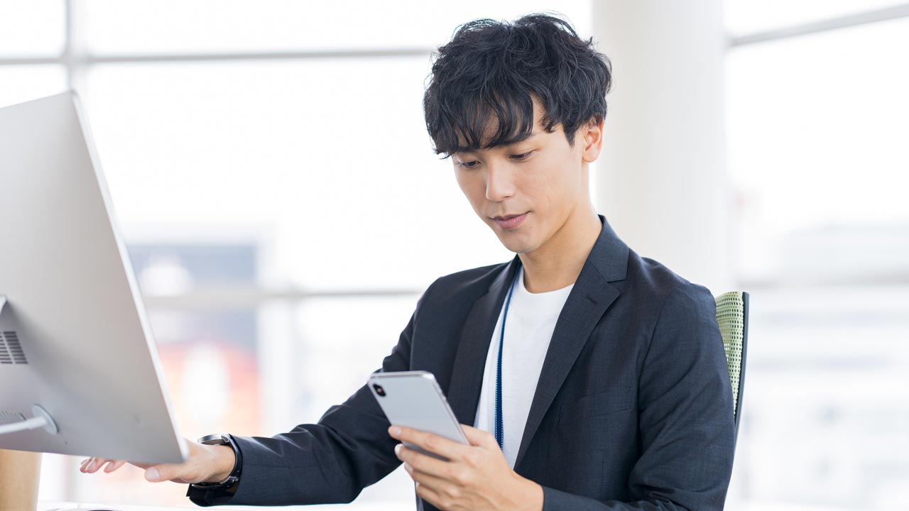 スマホを見るカジュアルなオフィスワーカーの画像